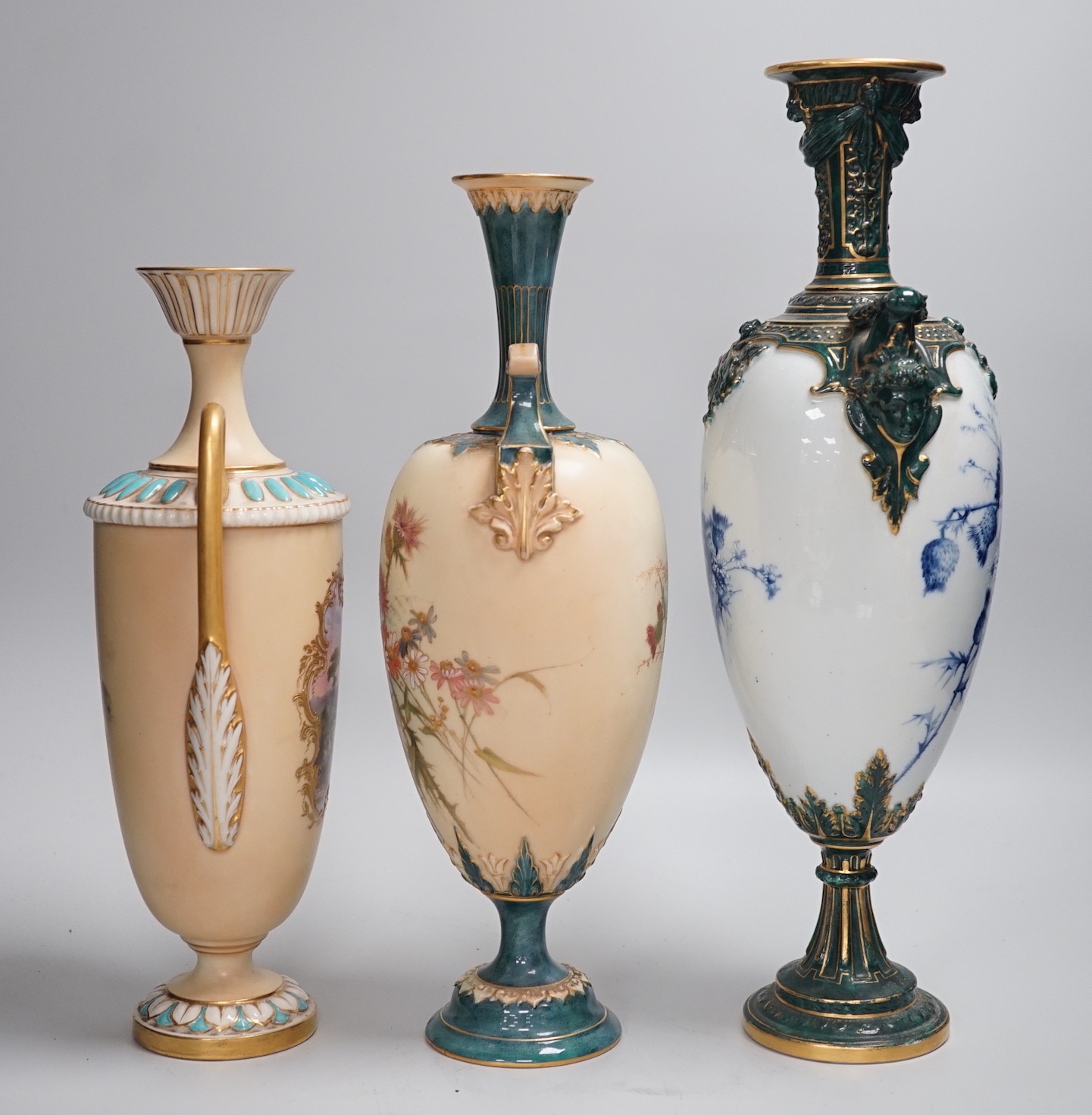 Three Royal Worcester pedestal vases, each of ovoid form and supported on circular pedestal feet, two are decorated with flowers and thistles, the other depicting a rural landscape within a gilt foliate C scroll cartouch